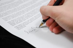 A close-up of a hand signing a contract using a black fountain pen