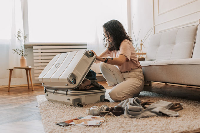 A woman crouching on a living room floor by an open suitcase