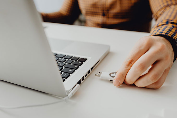 A close-up of a hand putting a white USB into a Mac computer.