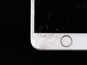 A close-up photo of the bottom left corner of a smashed white iPhone against a solid black background