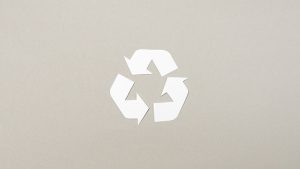 Three rotating arrows in the recycling formation. They’re cut out from white paper against a tan background