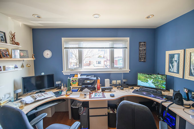 A photo of a blue-coloured home office. There's a wrap-around desk with two chairs, and computer monitors with a window in between