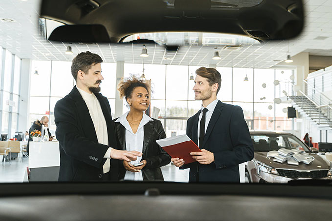 Couple at a car dealership discussing financial data with a salesperson